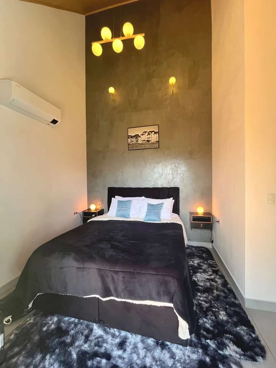 Quarto da Araucárias com cama de casal, luminárias acesas e ar-condicionado.