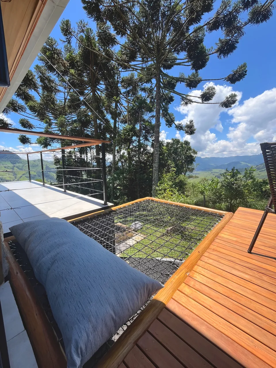 Rede de malha na varanda de madeira, entre araucárias e céu azul.