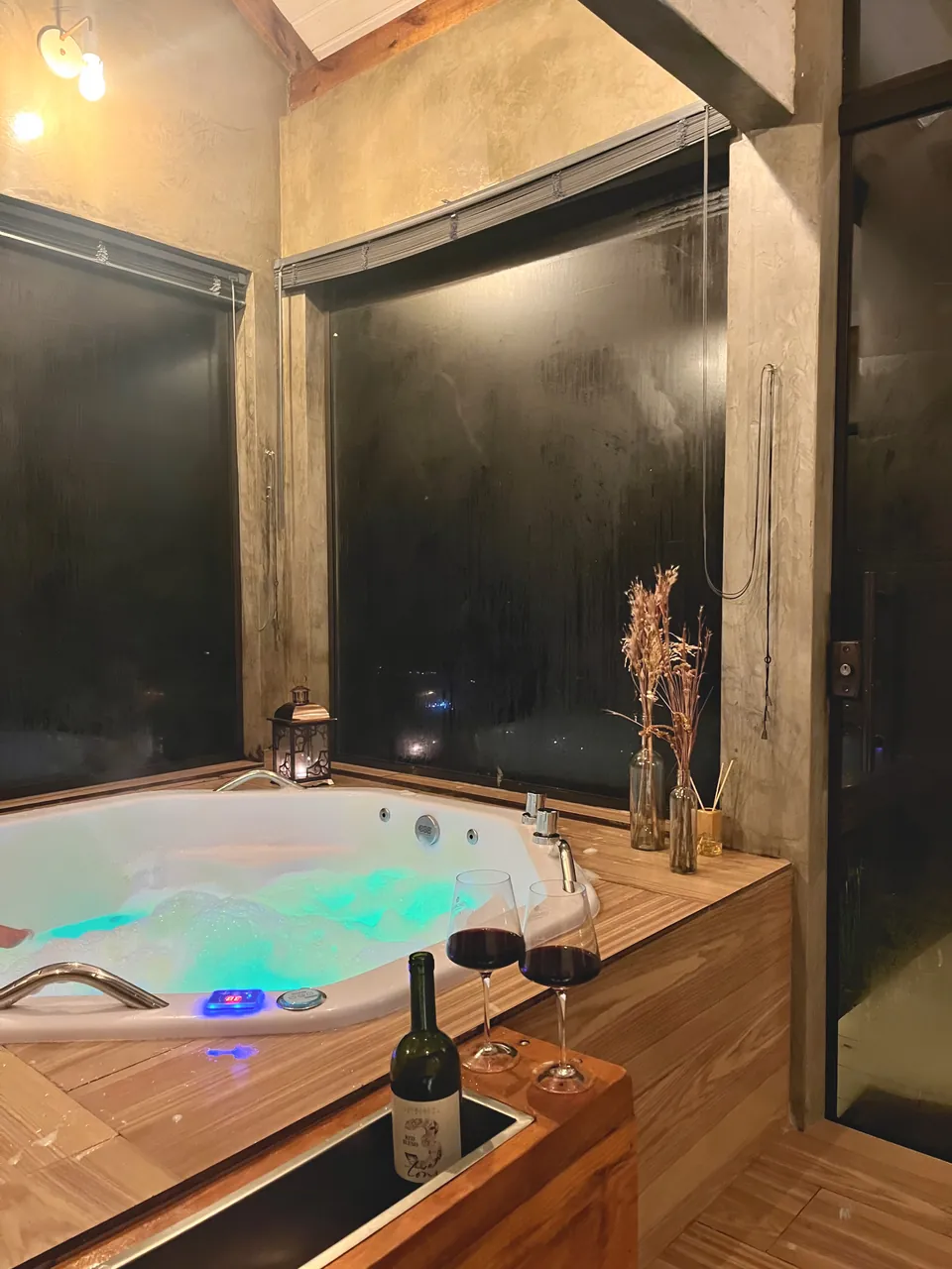 Banheira de hidromassagem iluminada, com taças e uma garrafa de vinho na borda de madeira.
