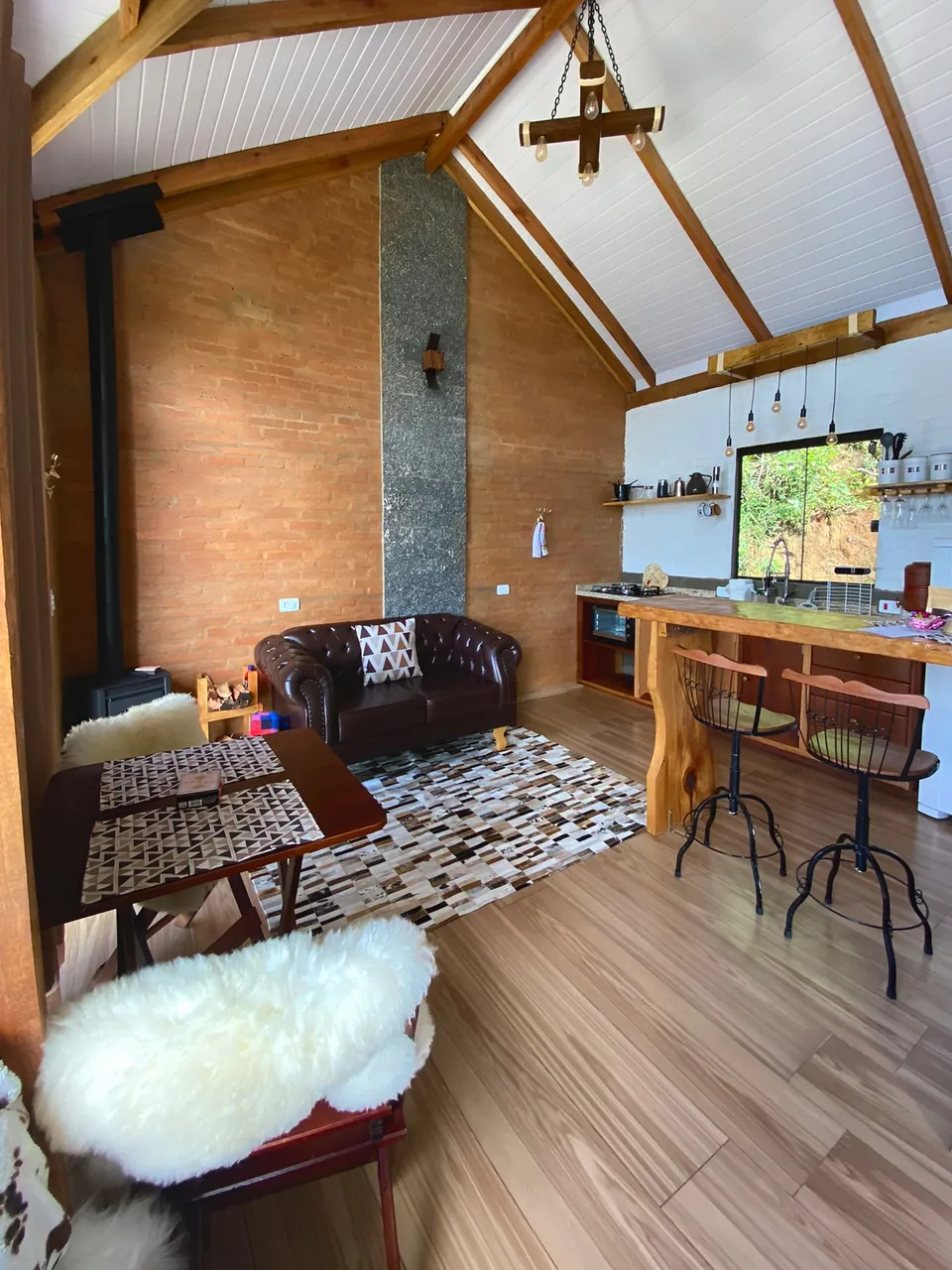 Sala e cozinha da Belvedere, com parede de tijolo, sofá de couro, bancada de madeira e teto alto.
