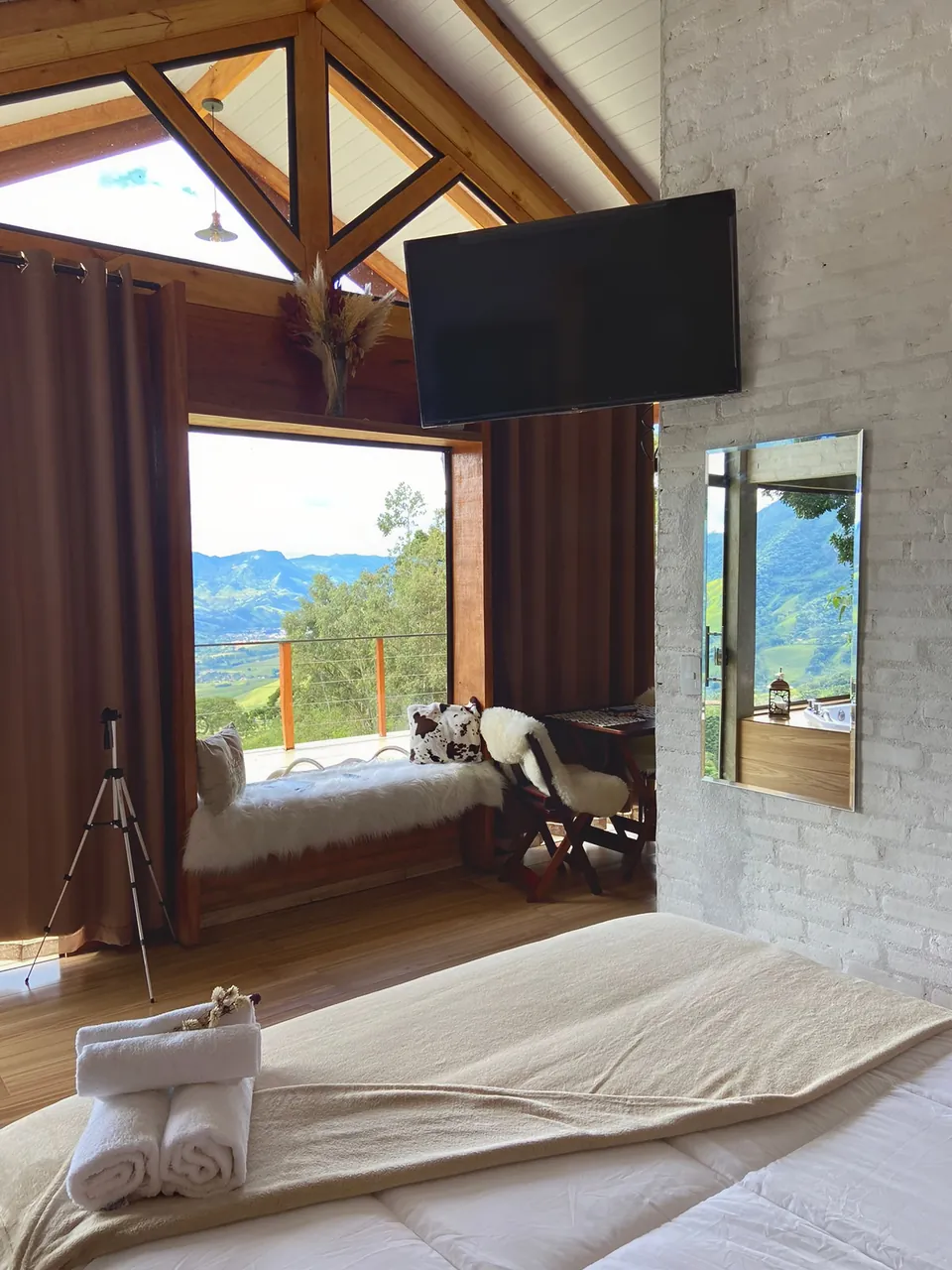 Cama da Belvedere com toalhas dobradas, de frente para a janela grande e a vista da serra.