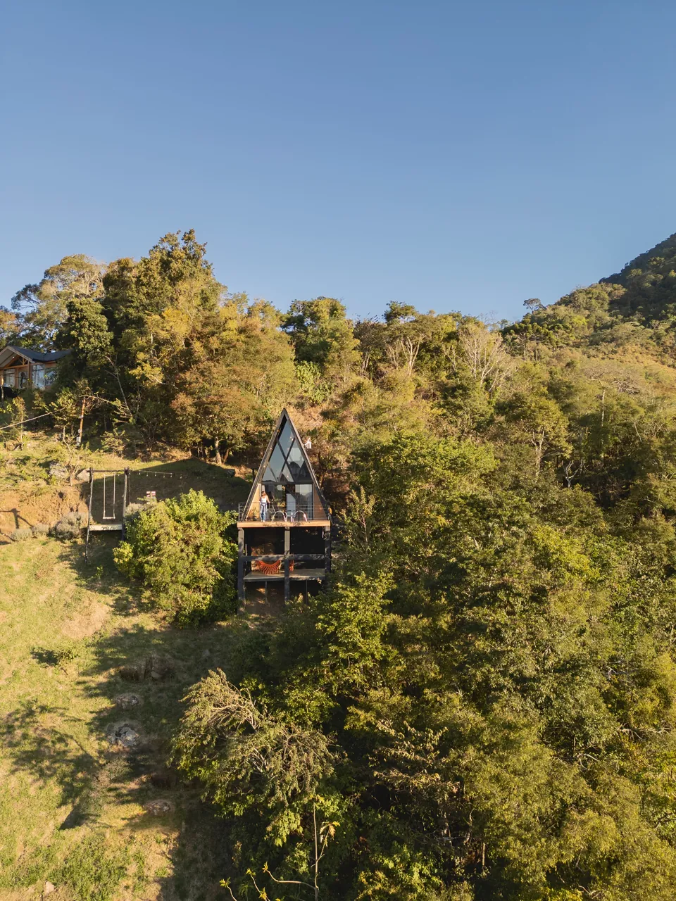 Das Pedras inteira na encosta, com o telhado em A, o deck e o balanço ao lado, entre a mata.