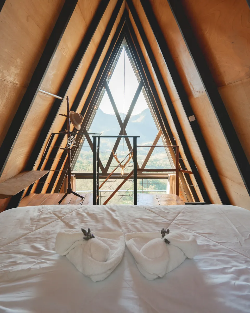 Cama da Das Pedras com toalhas dobradas, sob o telhado em A e a janela triangular para a serra.