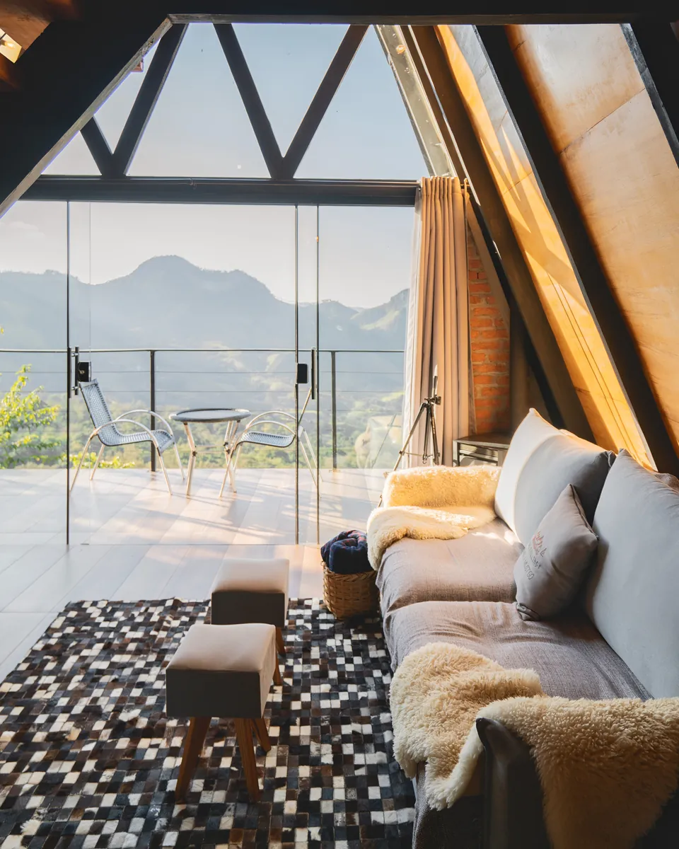 Sala da Das Pedras com sofá, pufes e tapete, aberta por portas de vidro para a varanda e as montanhas.