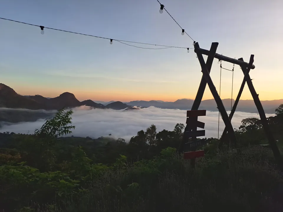 Balanço de troncos ao amanhecer, com varal de luzes e a névoa no vale.