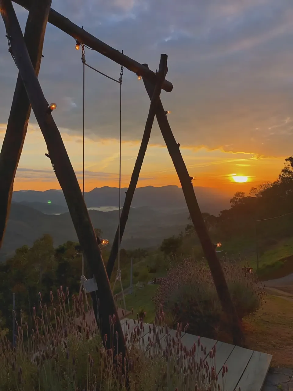 Balanço de troncos com luzes, com o sol se pondo atrás das montanhas.