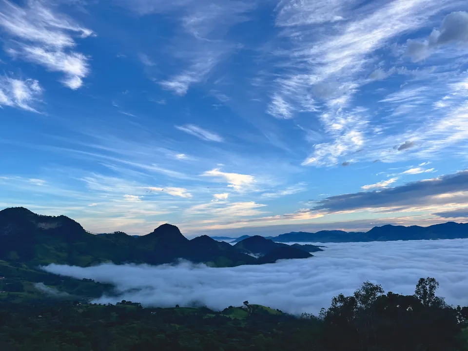 Mar de nuvens entre as montanhas, sob céu azul com nuvens altas.
