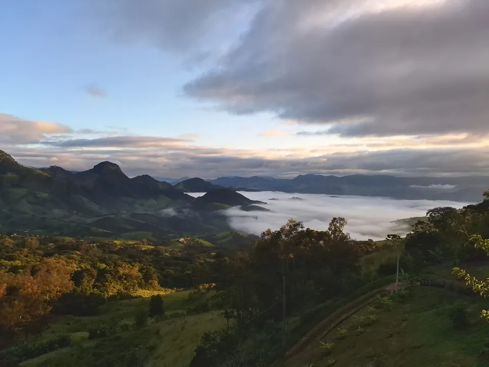 Vale com névoa e montanhas no fim da tarde, visto do alto do terreno.