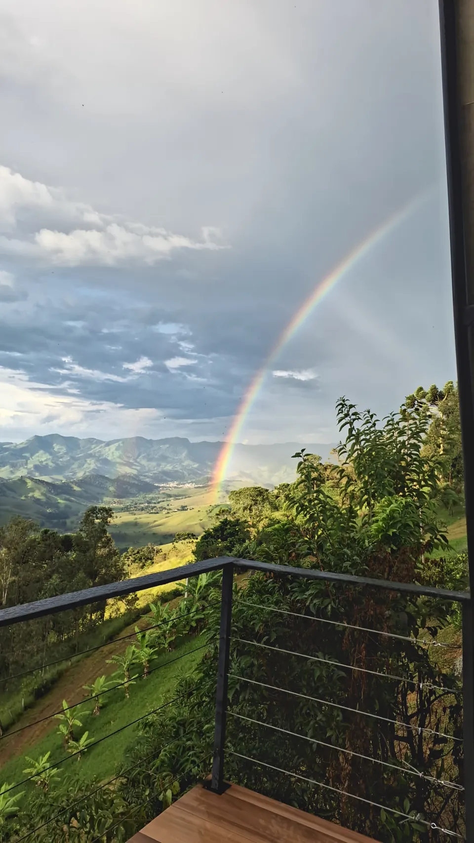 Arco-íris sobre o vale verde, visto de uma varanda com guarda-corpo.