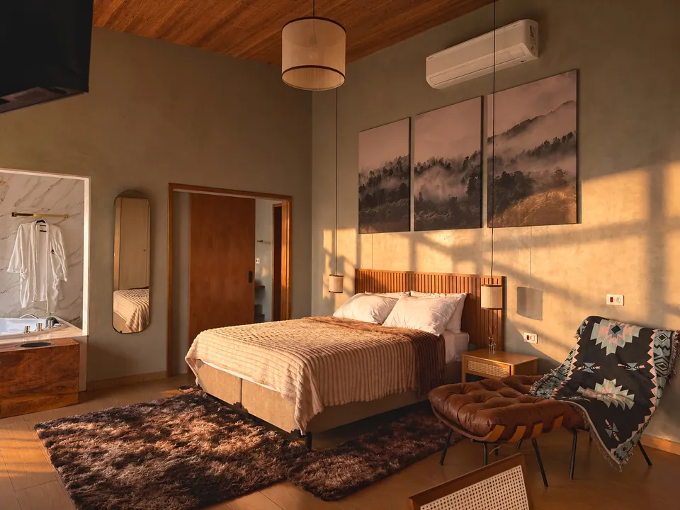 Quarto da Mantiqueira na luz da tarde, com cama de casal, poltrona de couro e tapete felpudo.