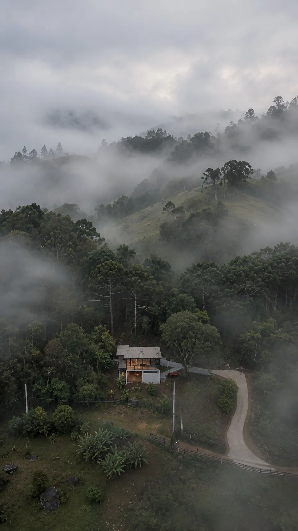 Vista aérea da Mantiqueira inteira entre a mata e a neblina, com a estrada de terra que chega até ela.