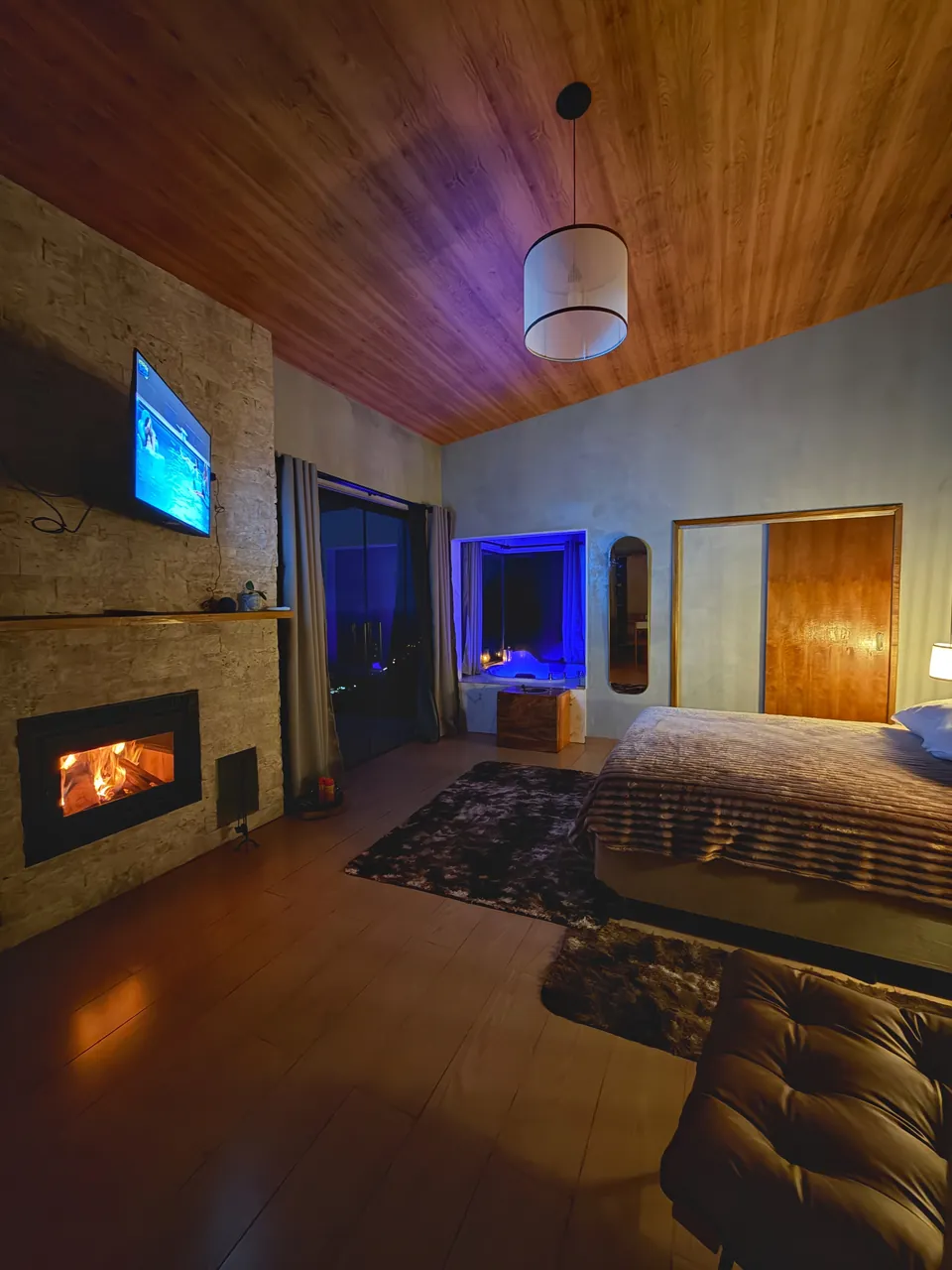 Quarto da Mantiqueira à noite, com a lareira acesa e a cama ao lado.
