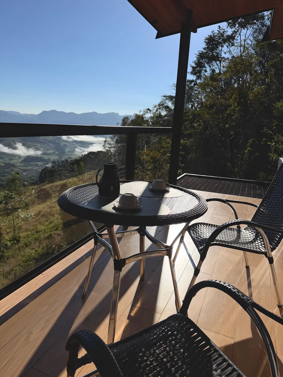 Mesa com café e cadeiras na varanda envidraçada, de frente para o vale.