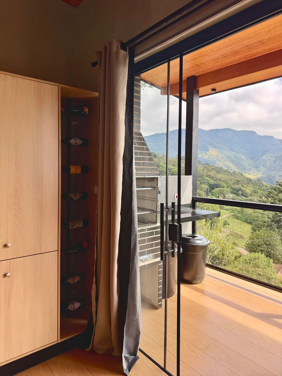 Adega de parede ao lado da porta de vidro aberta para a varanda e as montanhas.