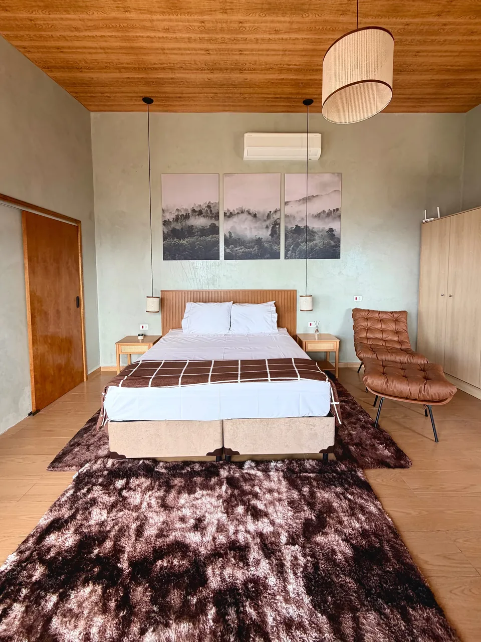 Cama de casal da Mantiqueira sob o forro de madeira, com quadros de montanha na parede.