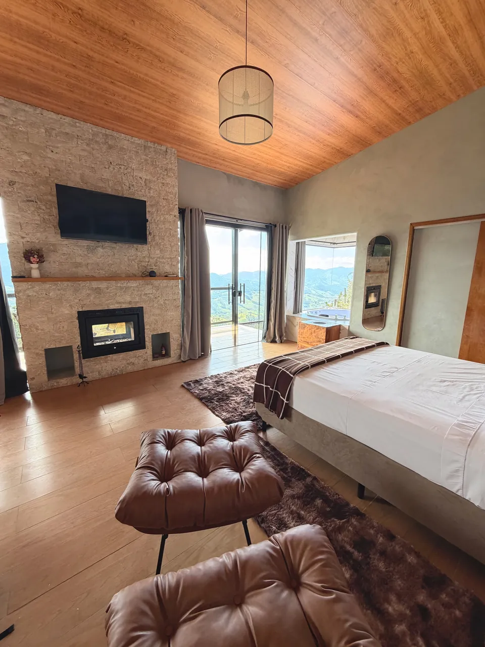 Quarto da Mantiqueira com forro de madeira, lareira na parede de pedra e portas de vidro para a varanda.